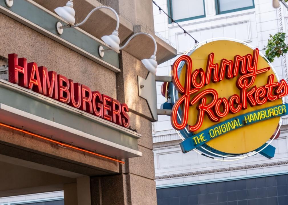 A Johnny Rockets sign attached the restaurant building, which also has the word hamburgers on it.