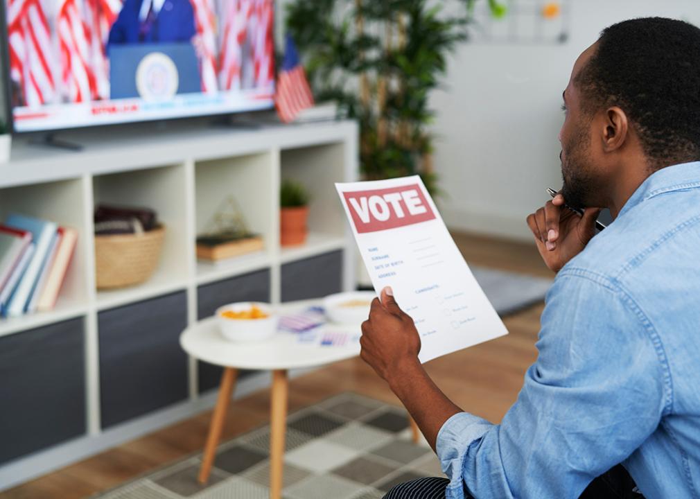 Man watching presidential elections news at home while holding a voting guide.