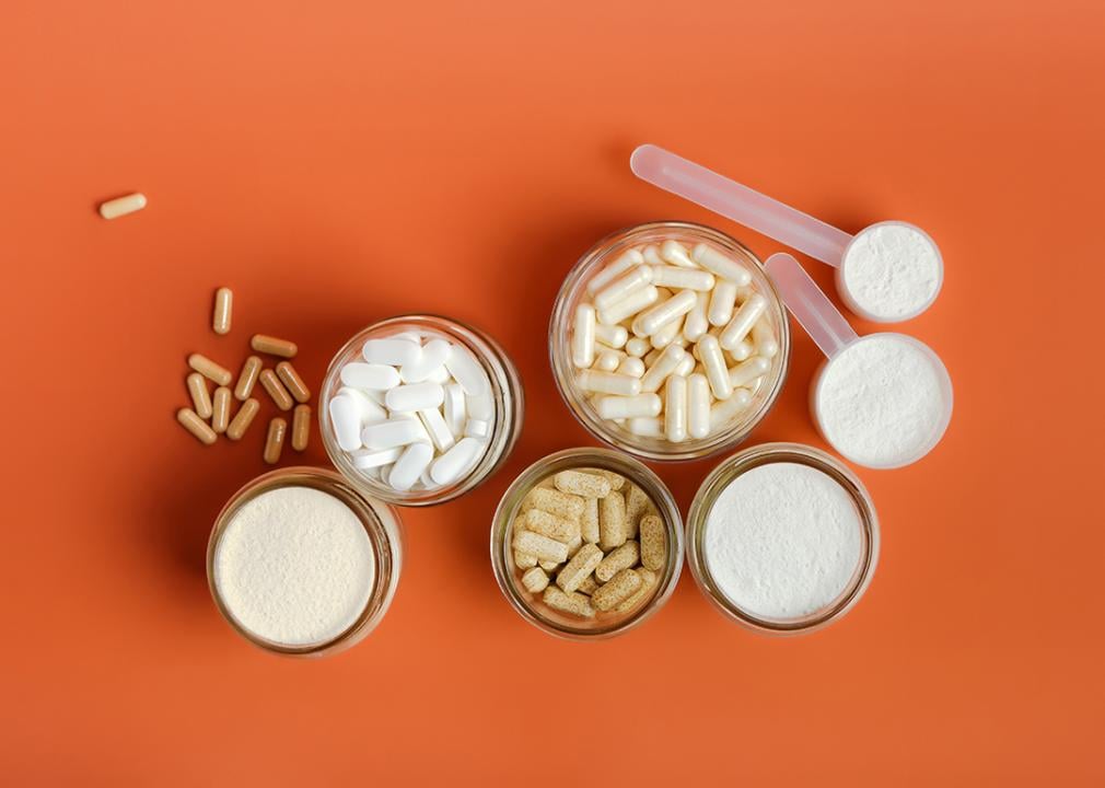 Flatlay of different types of vitamins, supplements and protein powder displayed with an orange background.