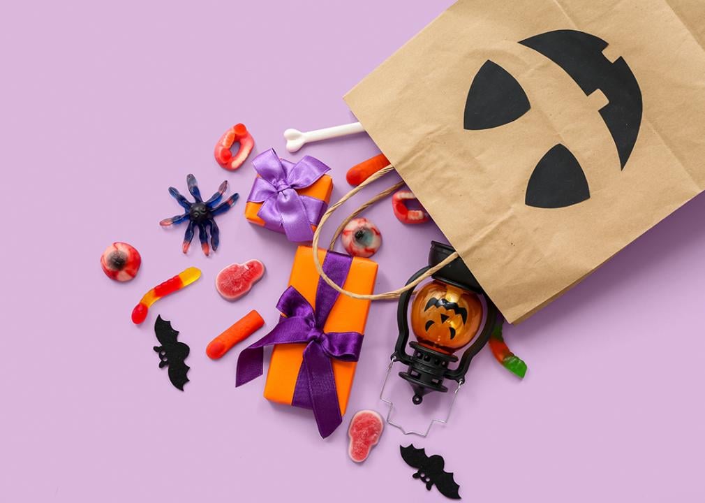 Halloween shopping bag with candies and gifts on a lilac background.