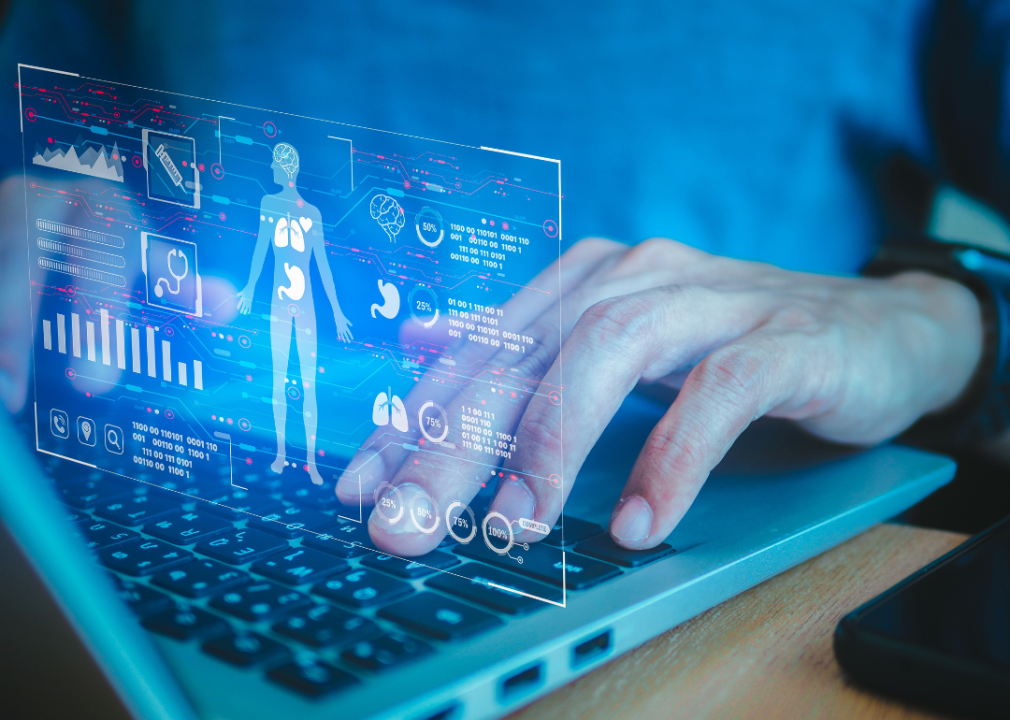 Hands typing on a laptop with an overlay of a virtual health care profile floating above the keyboard.