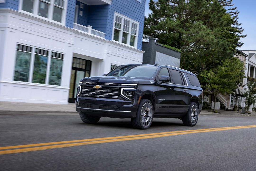 Dark Chevy Suburban driving past blue and white building on road.