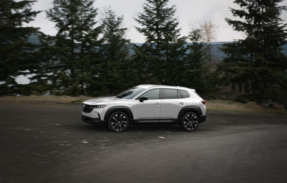 White Mazda CX 50 driving on a road in the forest.