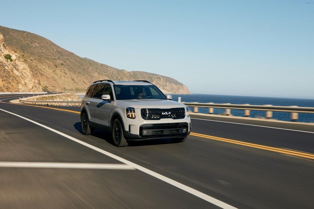 Photo of light-colored Kia Telluride driving near the beach on road.