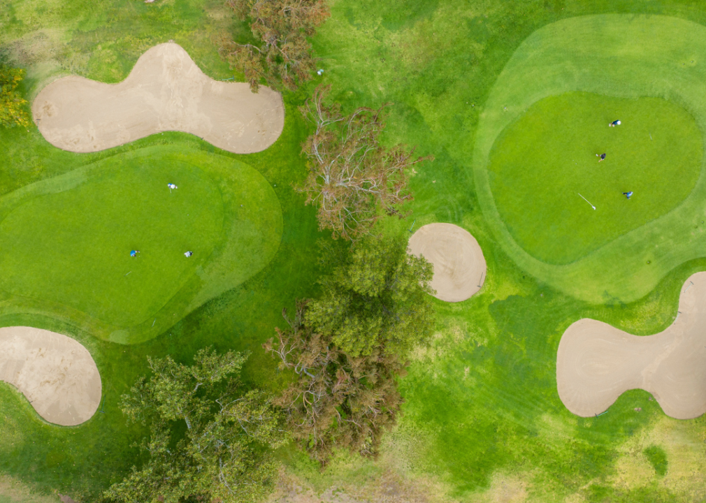 An aerial view of a green golf course with dry patches and trees.