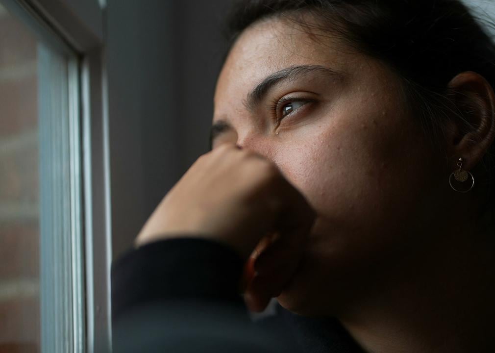 A pensive young woman sitting by a window looking outside.