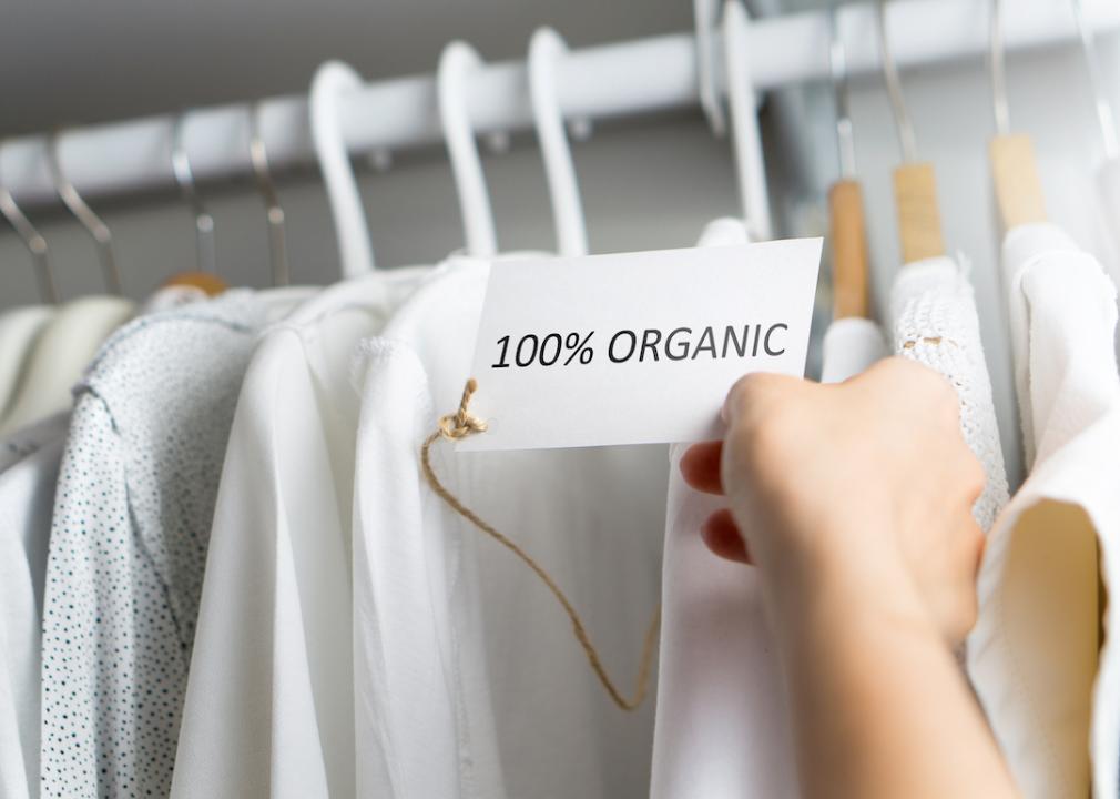 A person looks at a 100% organic tag on a clothing rack of shirts. 