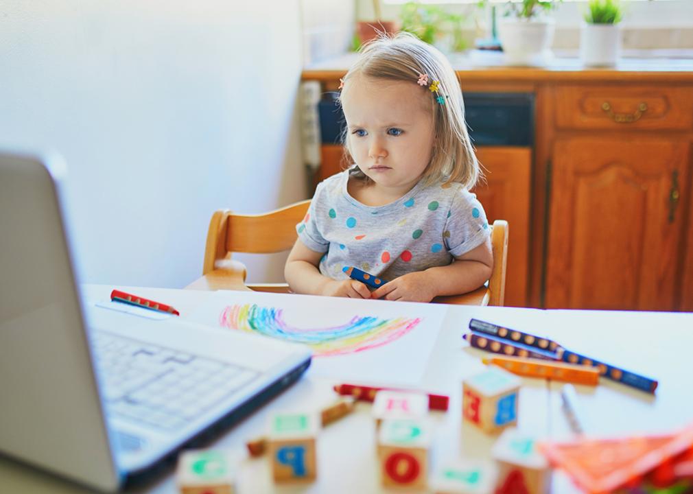 A toddler girl focused on watching in front of a laptop.