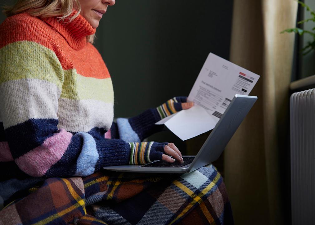 A woman sitting by the radiator is looking at her energy bill and looking up information using a laptop.