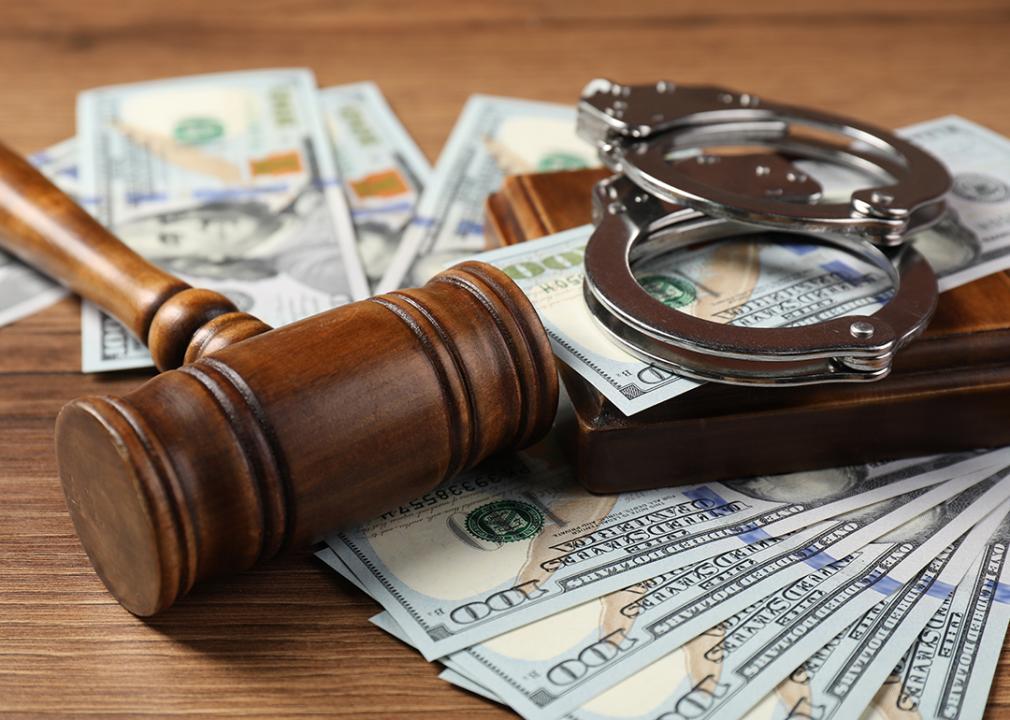 A closeup on a judge's gavel, money and handcuffs on a wooden table.