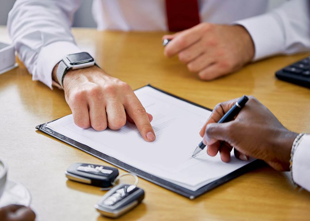 Close-up photo of hands and paperwork for financing a car with car keys visible.