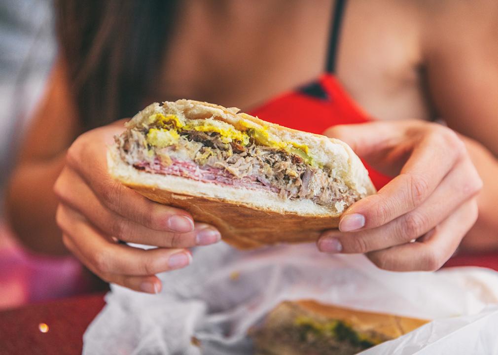 Closeup of a woman holding a Cuban sandwich at a typical local cafe outdoors. 