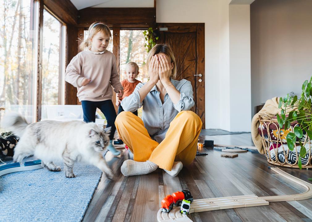 Stressed out mother sitting on the floor while kids are playing around.