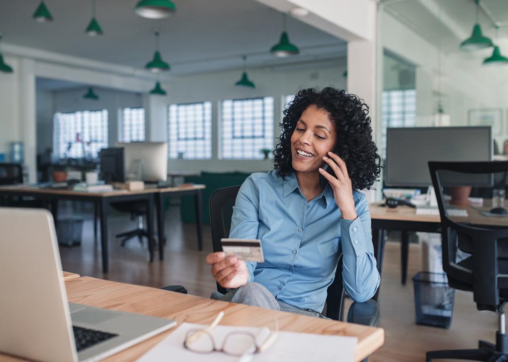 A young businesswoman smiling while on the phone and looking at her credit card.