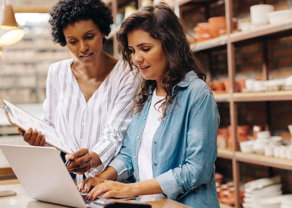 Two small business owners going through expenses, ceramics and products visible on shelves behind them.