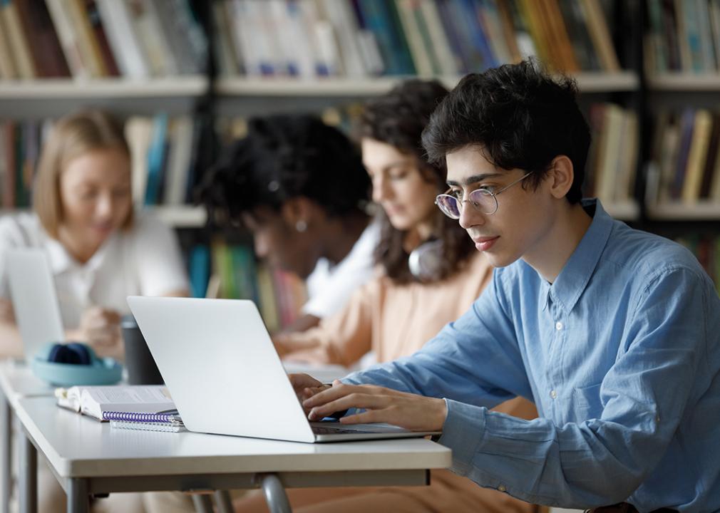 A row of students sitting at table in the library working on laptops.