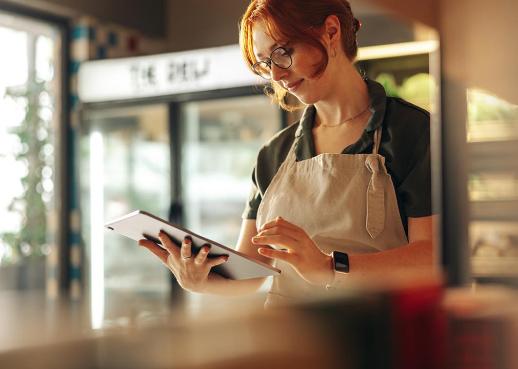 A small grocery owner using a digital tablet in her store.