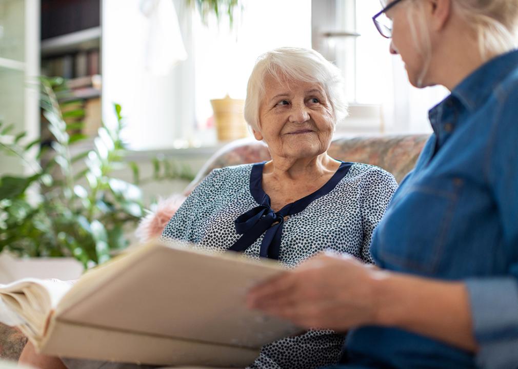 An elderly woman looking through an old photograph book with her adult daughter.