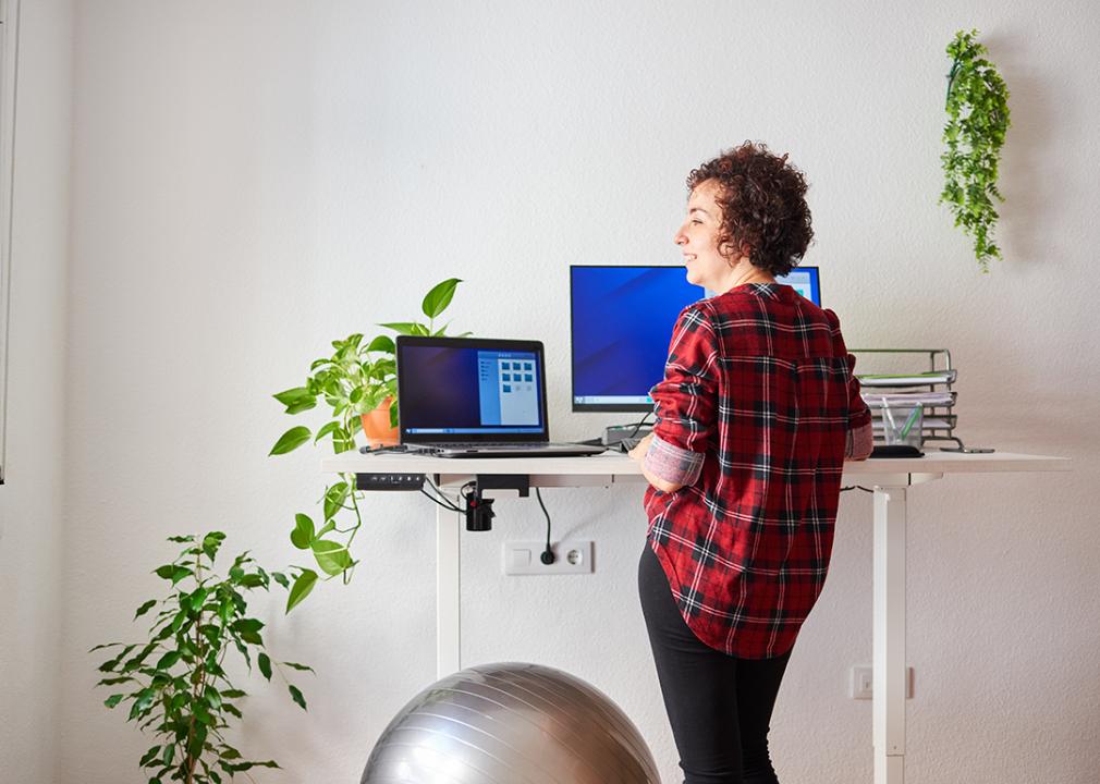 Woman working from home with an adjustable desk standing next to a fitness ball.