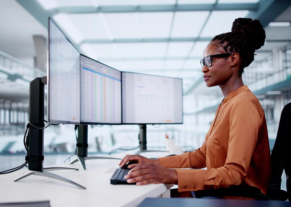 Accountant using three monitors to organize invoices using a software.