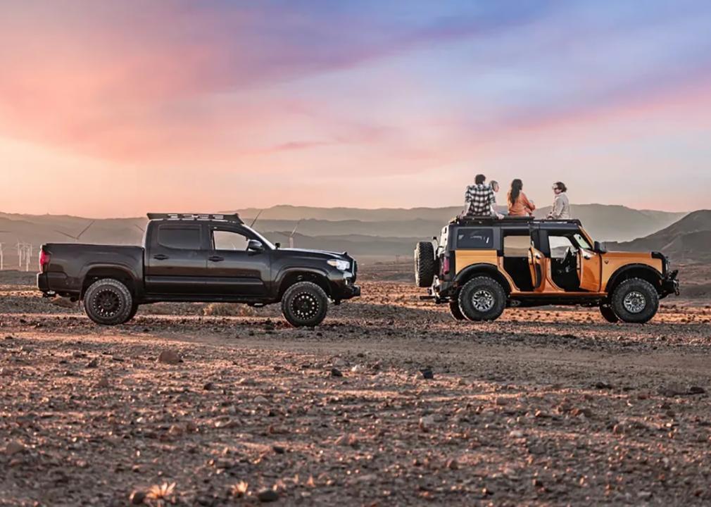 An AWD and a 4WD vehicle on a wide park lot with its passengers watching sunset.