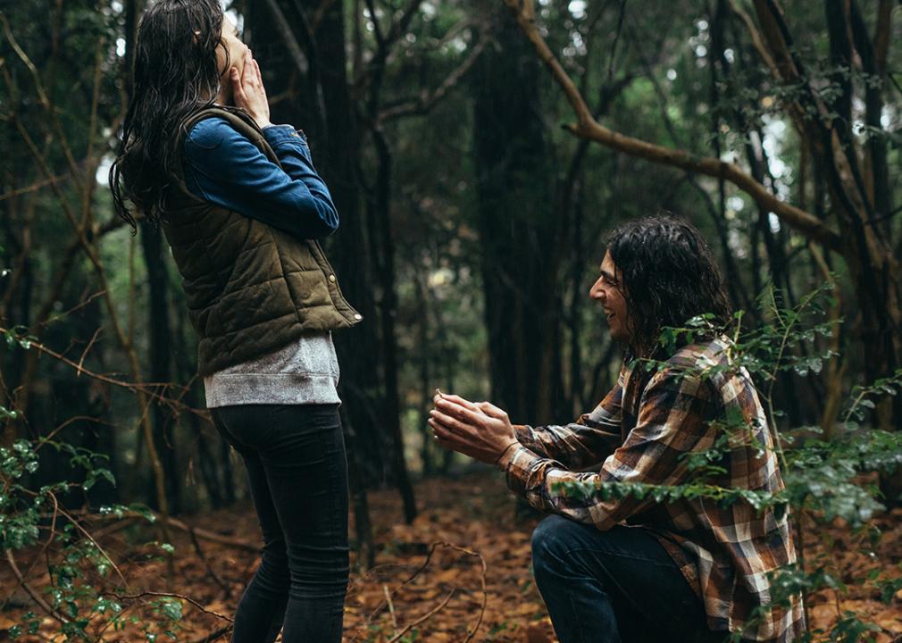 A man proposes to his partner during a rain in a natural location.