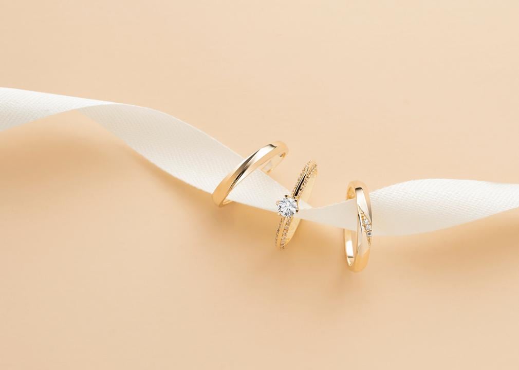 A white ribbon holds three types of different wedding rings.