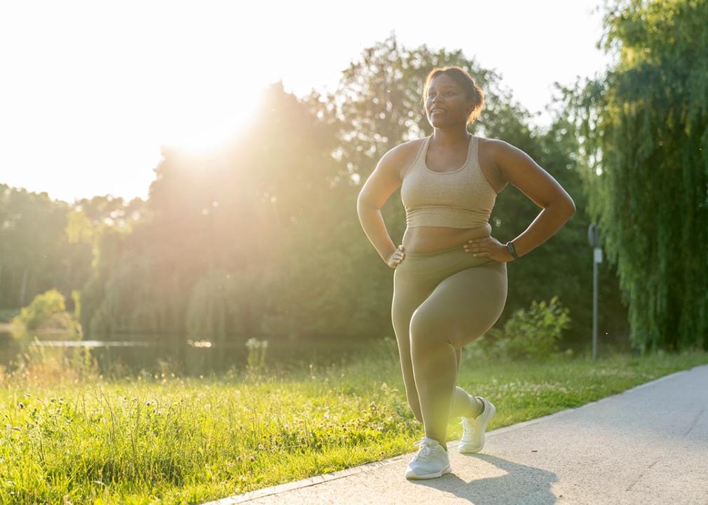 Woman doing a lunge in a park, backlit by sun with grass in the background.