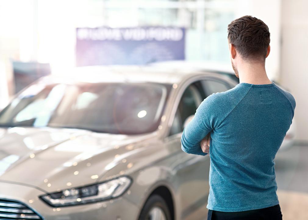 A thoughtful man who looks at a car in a dealer.