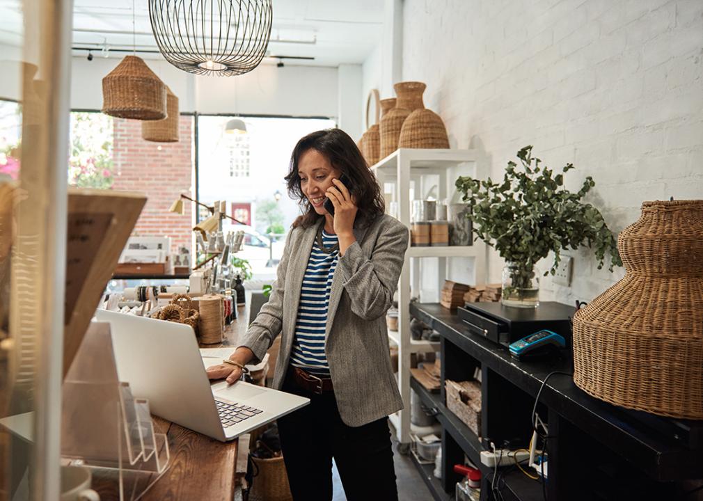 A small business owner looking at her laptop and talking on the phone behind the counter in her boutique.