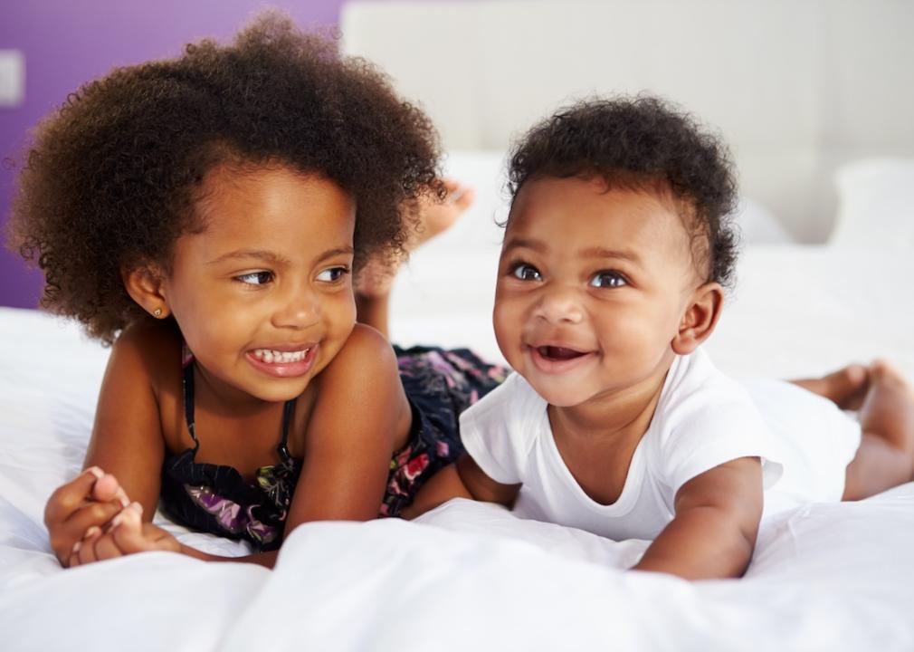 A baby girl and baby boy laying together on a bed.