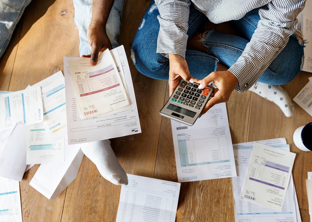 Two people on the floor managing debt by calculating invoices, bills and expenses.
