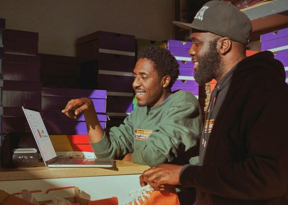 Two members of a shoe retail shop looking at a sales report from a laptop.