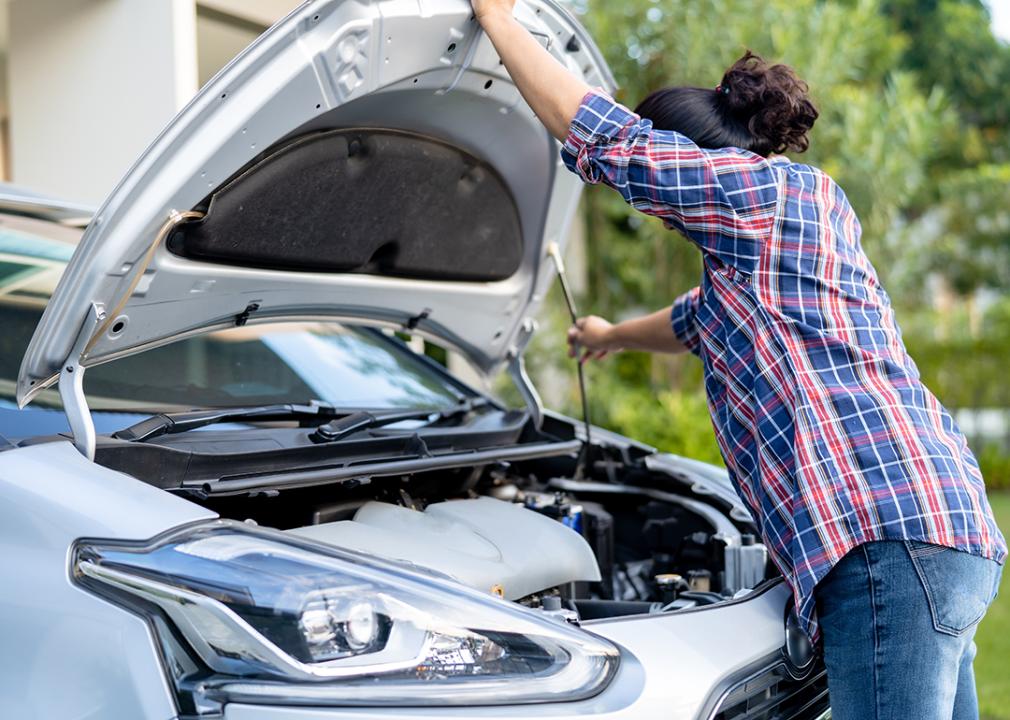 A female car owner opening the hood of her silver car to inspect its engine.