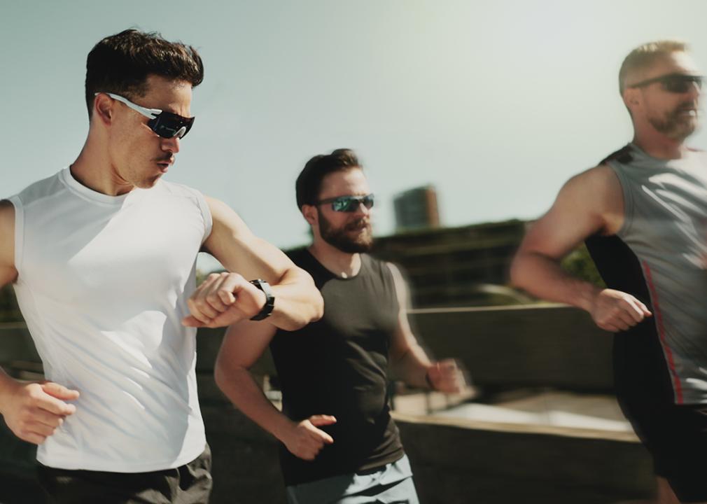 Three men on a fitness run and one of them is looking at his smartwatch for tracking.
