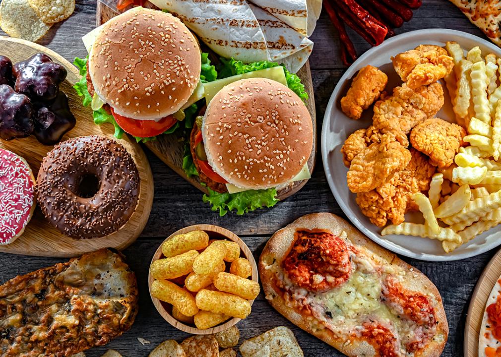 Trays of fast food such as donuts, burgers, chicken nuggets, fries and pizza.