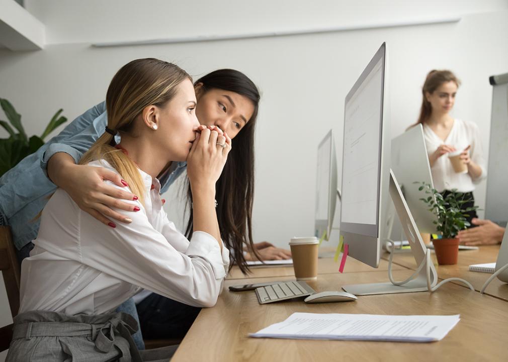 A woman at work reading bad news from email and her colleague is holding her for support.
