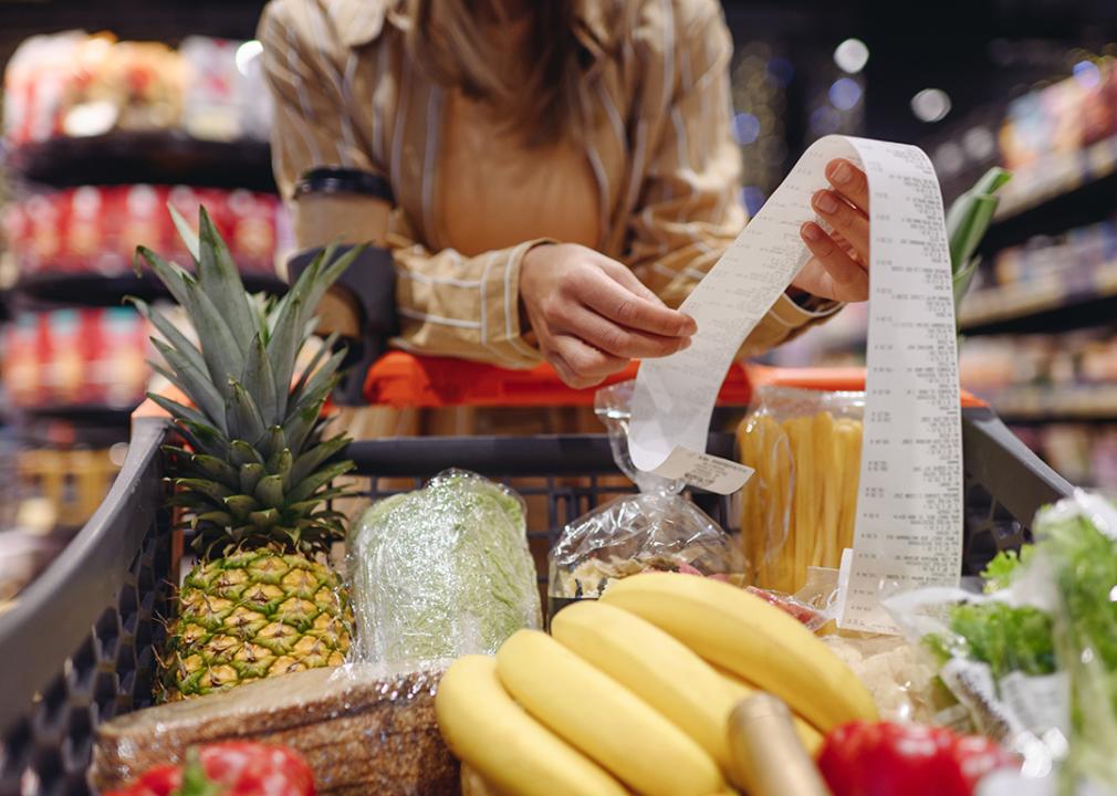 Woman leaning on a grocery cart while reading the receipt of her purchases.