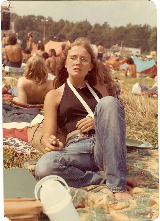 "My mom at at an Allman Brothers concert with a broken arm. Watkins Glen, 1973." A young woman with her arm in a sling laying in a field at a concert