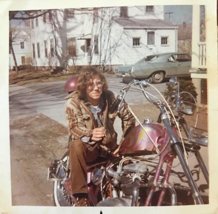 "My dad sitting on the back of his motorcycle before his high school graduation in 1973." A young man sits on a pink motorcycle in a driveway