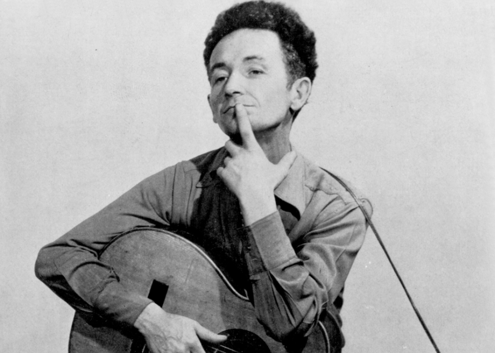 Woody Guthrie poses for a portrait with his guitar.