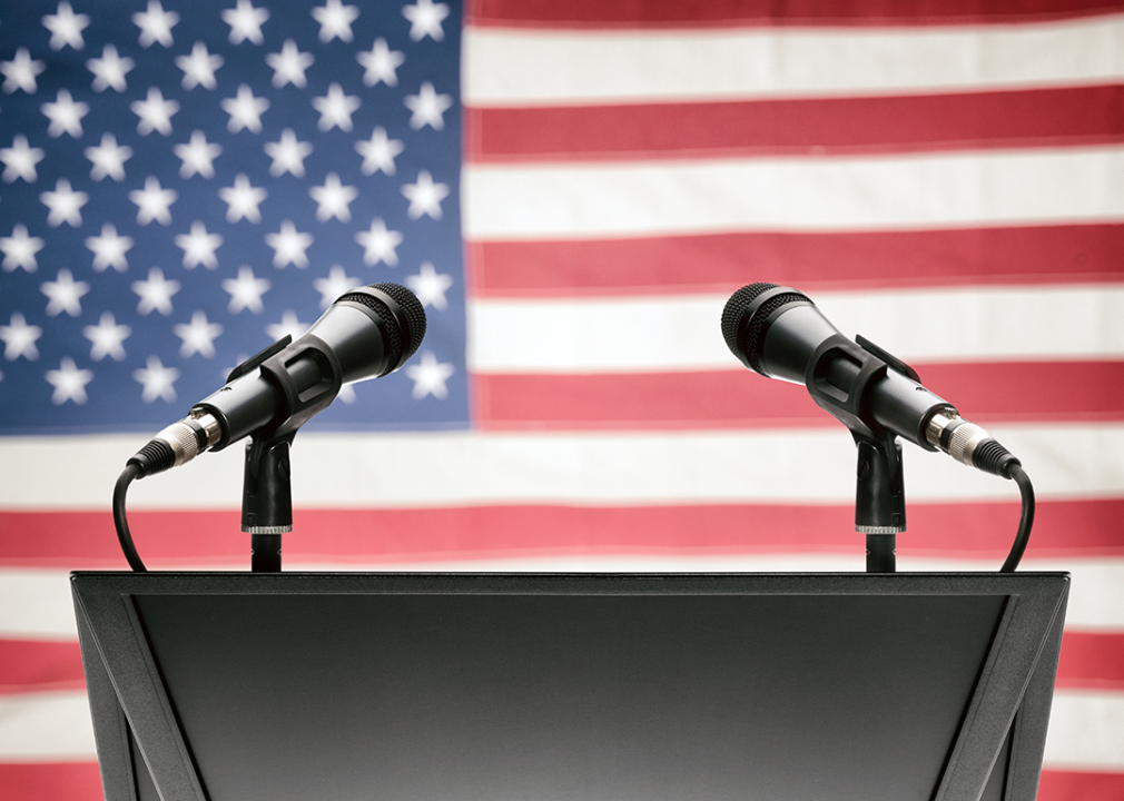Speech podium with two microphones and American flag.