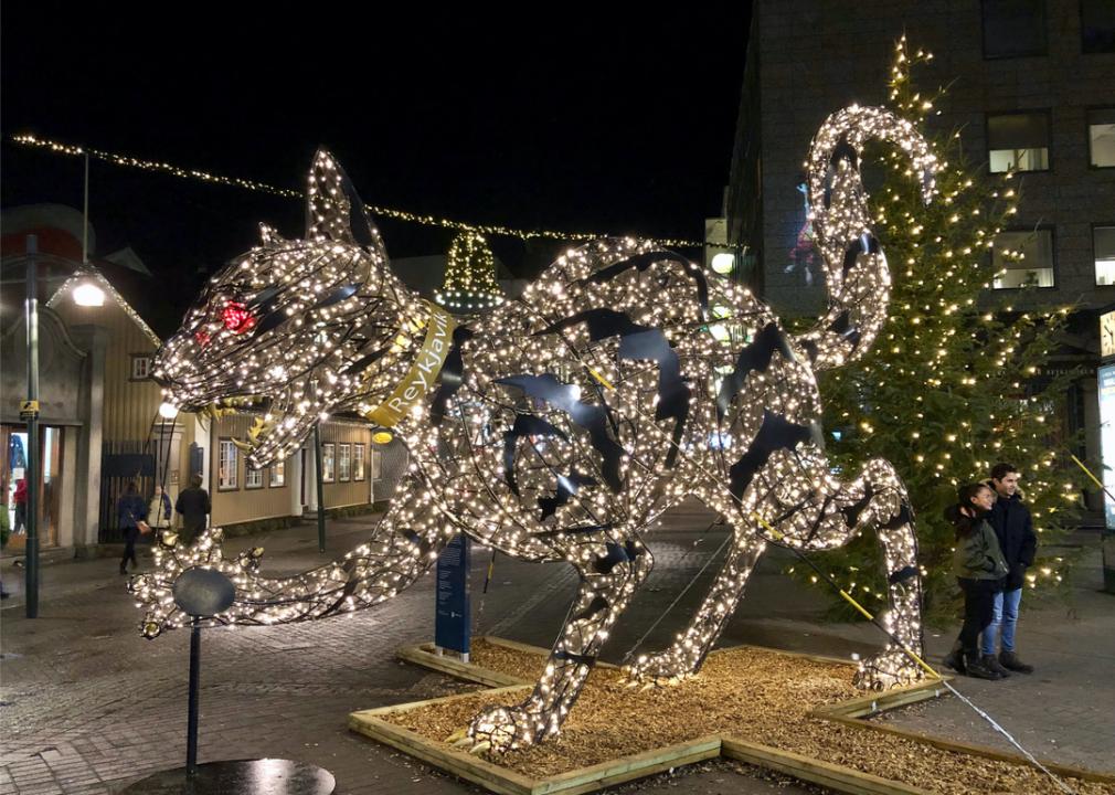 A very large, lit up cat figure with red glowing eyes, and sharp teeth and claws with a Christmas tree in the background.