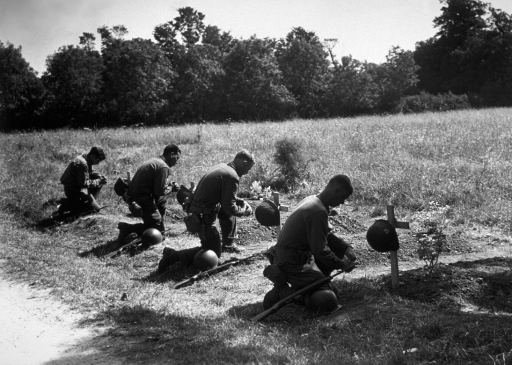 American soldiers kneel at the graves of their fallen comrades near Sainte Mere Eglise, France.