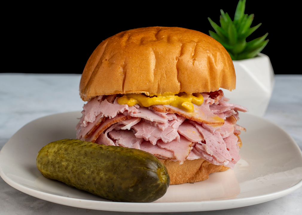Ham topped with mustard on a bun with pickle.