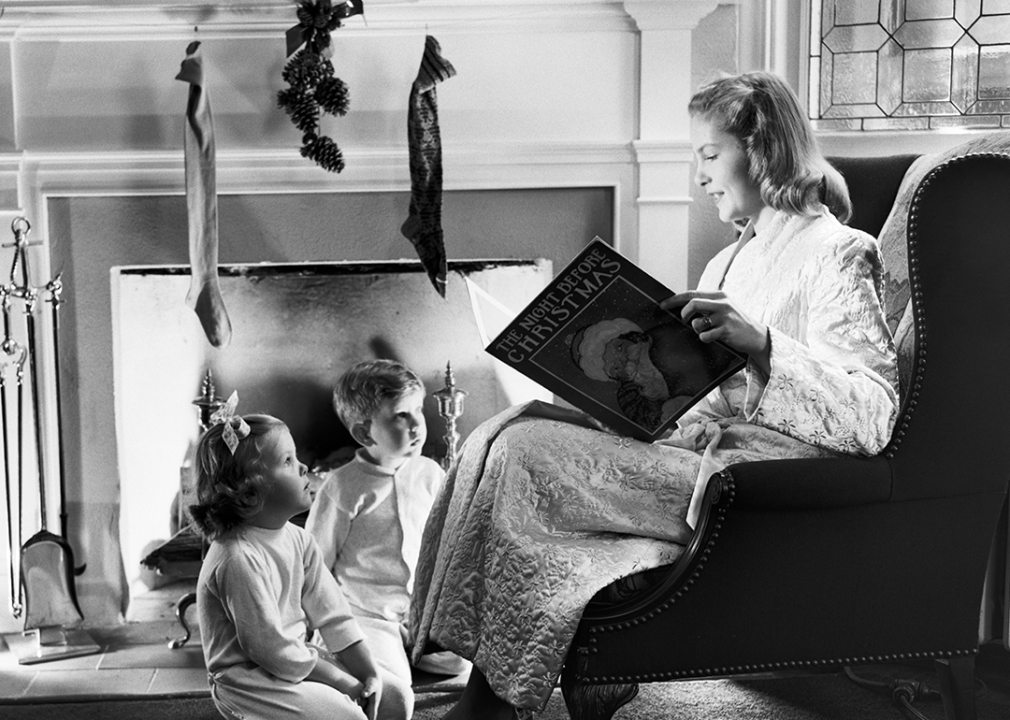 Mother reading Christmas story to children by the fire.