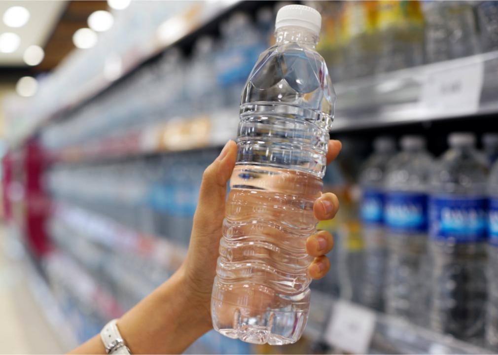Photo shows a close-up of a hand taking a bottle of water from a store shelf