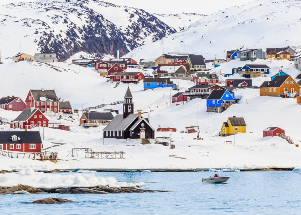 Brightly colored houses and buildings near icy waters and surrounded by snowy mountains.