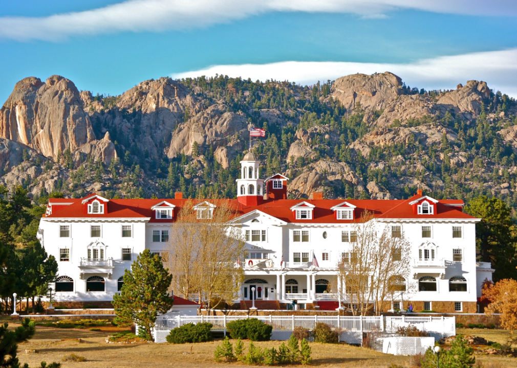 The Stanley Hotel, a large white building with red roof with rocky mountains in the background.