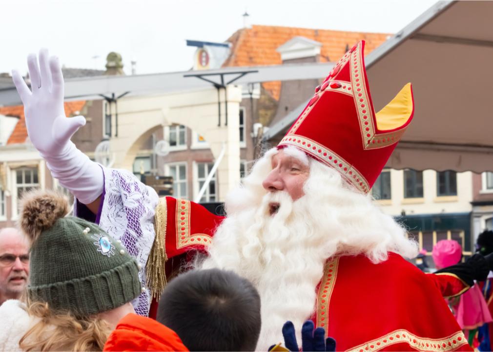A man dressed as a Santa Claus looking character waving to crowds.
